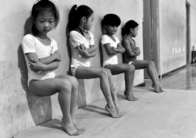 23- Fotografía ganadora del segundo premio de la categoría “Vida Cotidiana”, tomada por el fotógrafo Tiejun Wang. En la imagen, llamada “El sudor fabrica campeones”, aparecen cuatro estudiantes de la escuela de gimnasia que realizan flexiones de pie durante un entrenamiento de media hora en Xuzhou (China).